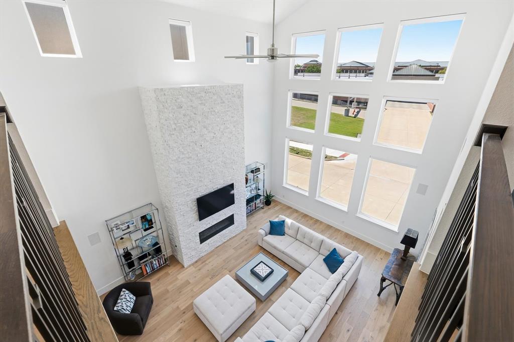 Vaulted ceilings featuring expansive floor-to-ceiling windows, white stone-textured fireplace surround, built-in linear fireplace, and wood-finish flooring