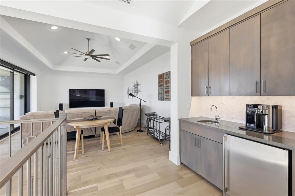 Wet bar featuring custom wood cabinetry, under-cabinet lighting, a stone-surfaced countertop, and a stainless steel under-counter refrigerator