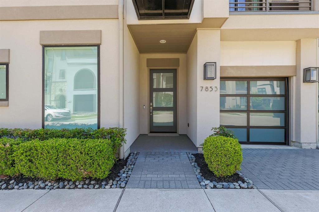 Contemporary exterior entrance featuring a modern glass-panel entry door, multi-pane frosted glass garage door, structured hedges, and a paver stone walkway Contemporary exterior entrance featuring a modern glass-panel entry door, multi-pane frosted glass garage door, structured hedges, and a paver stone walkway