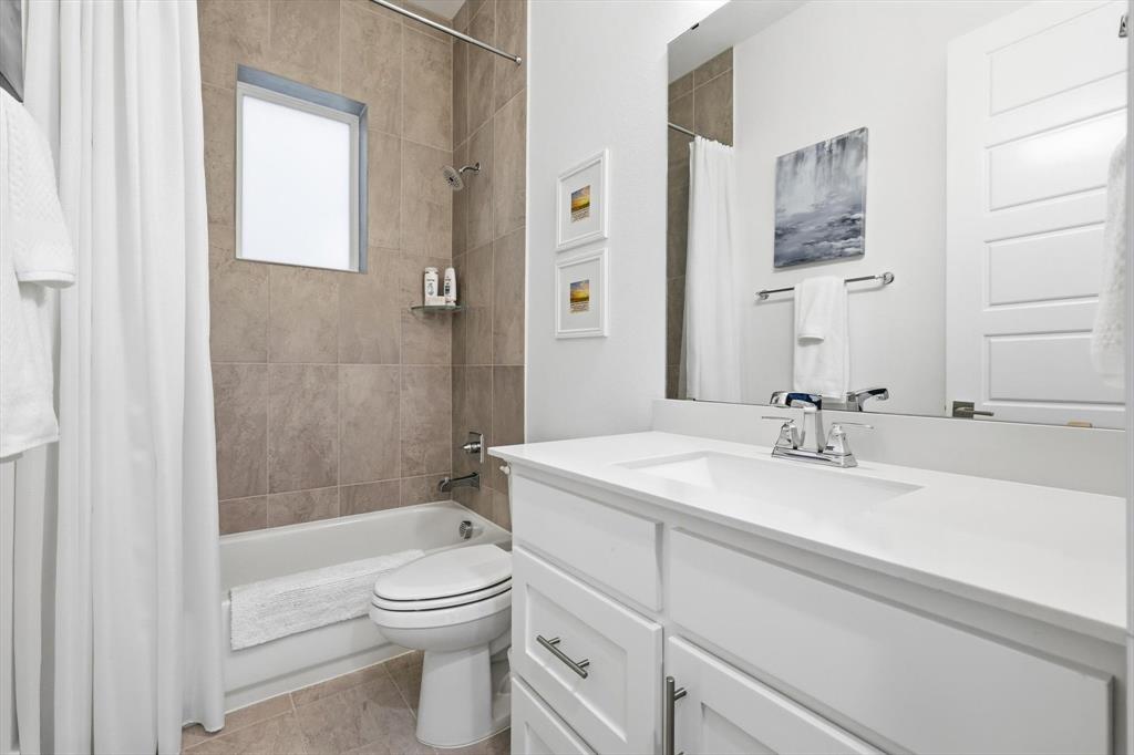 Bathroom featuring a white vanity cabinet with a solid surface countertop, rectangular under-mount sink, chrome hardware, large vanity mirror, and a tub-shower combination with floor-to-ceiling tile surround