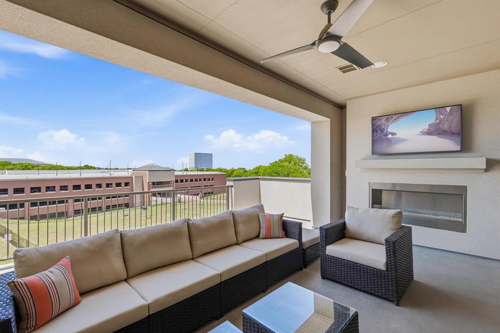 Covered balcony featuring a sleek, horizontal gas fireplace, mounted television, ceiling fan, and metal railing