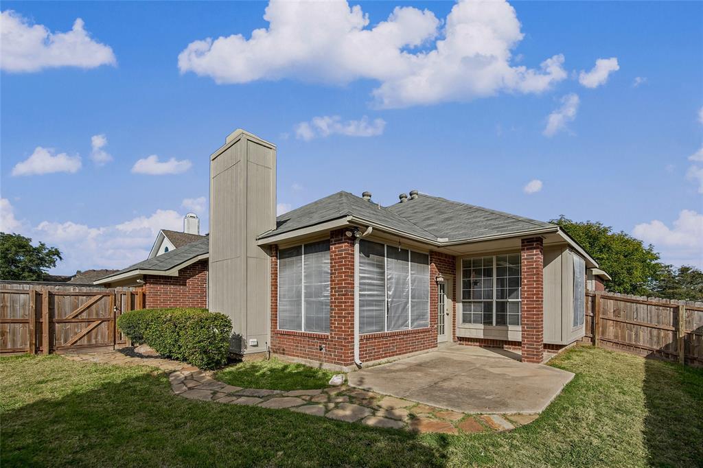 Rear exterior featuring brick siding, a concrete patio, a tall brick chimney, and a wooden privacy fence enclosing the grass yard
