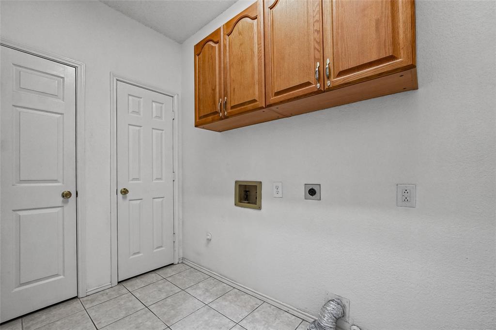 Utility area featuring tile flooring, wood-finish wall-mounted cabinetry, and dedicated washer and dryer hookups