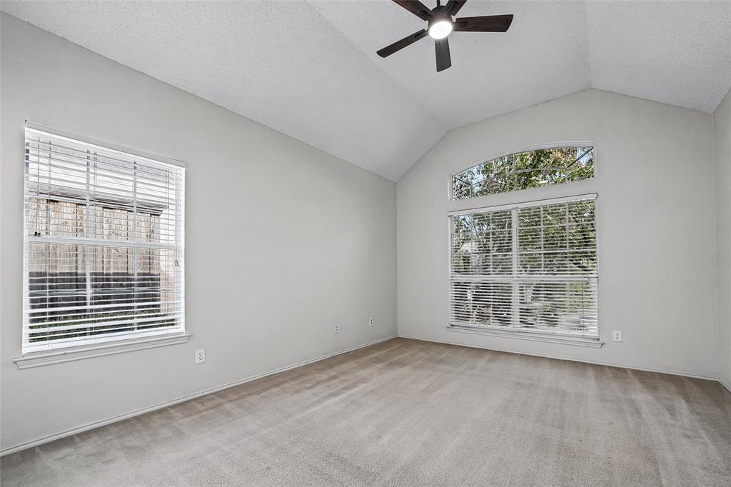Vaulted ceilings featuring a central ceiling fan, arched transom window, and neutral carpeting