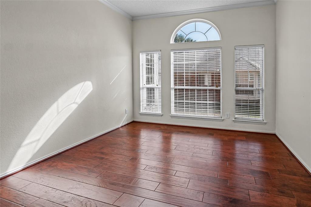 Wood-finish flooring, high ceilings with crown molding, and an arched transom window above a triple-window configuration with integrated blinds