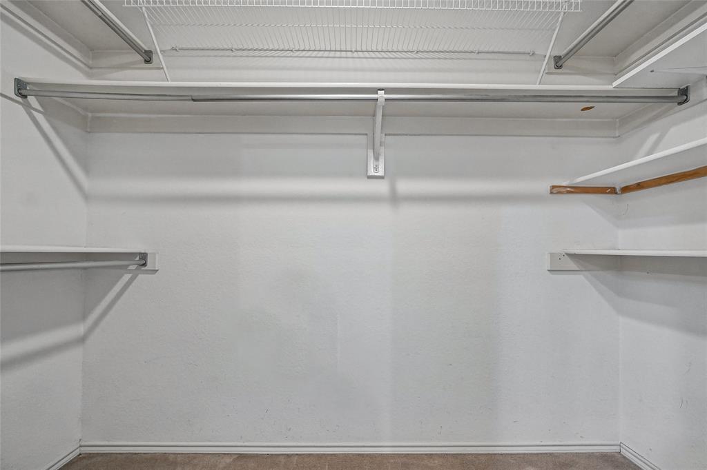 Walk-in closet featuring multi-level metal hanging rods and white fixed shelving