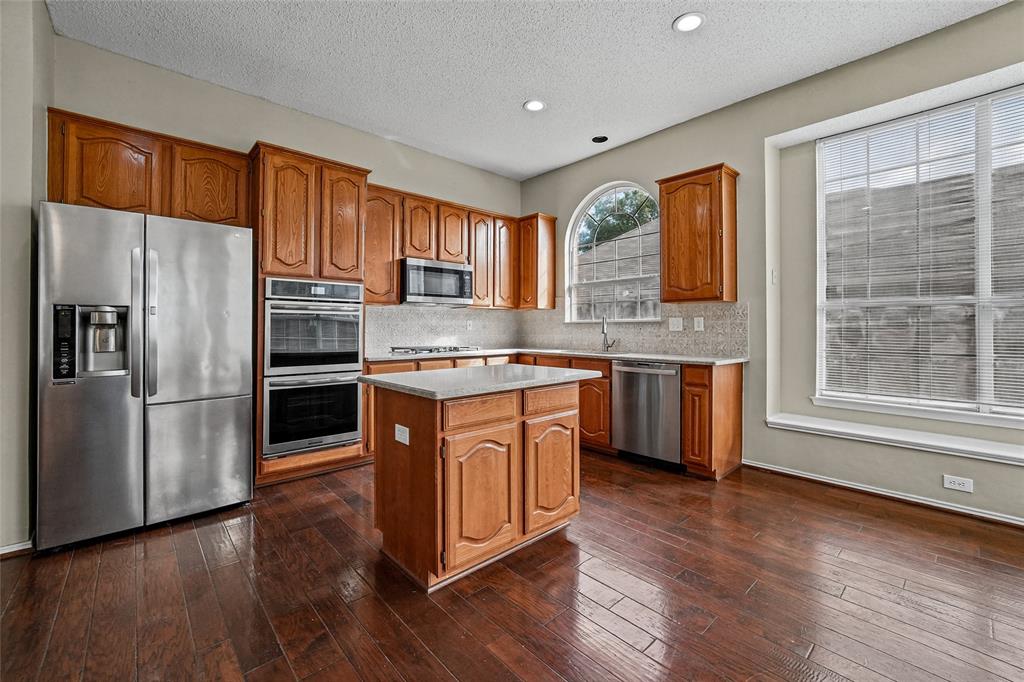 Kitchen featuring wood cabinetry, stainless steel appliances, central island, arched window, and wood-finish flooring