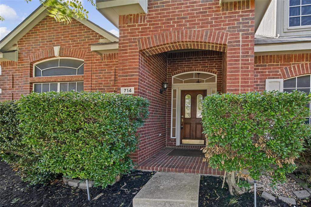 Red brick exterior featuring an arched entryway, recessed porch, wood-paneled door with glass inserts, and decorative transom windows
