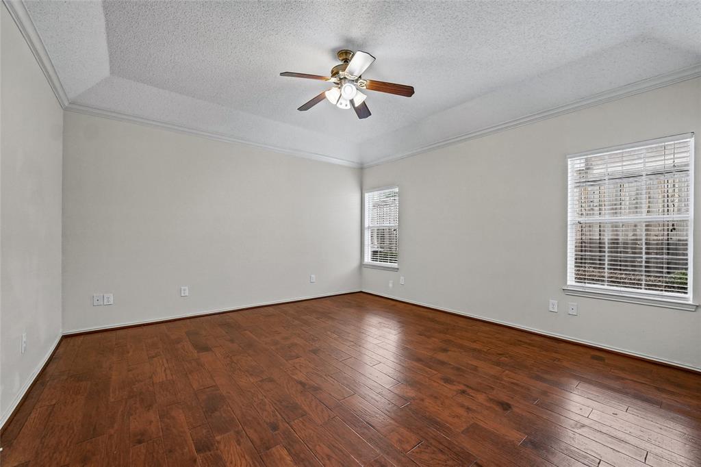 Tray ceiling featuring crown molding, wood-finish flooring, and a multi-blade ceiling fan with integrated lighting