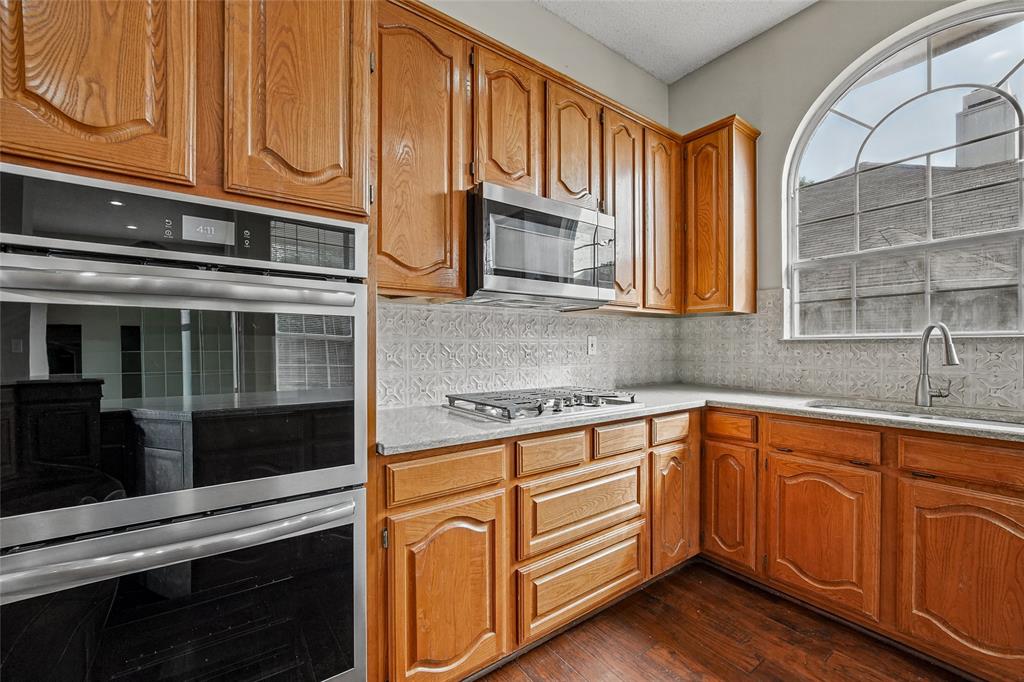 Kitchen featuring wood cabinetry, stainless steel built-in double ovens, gas cooktop, arched window, and wood-finish flooring