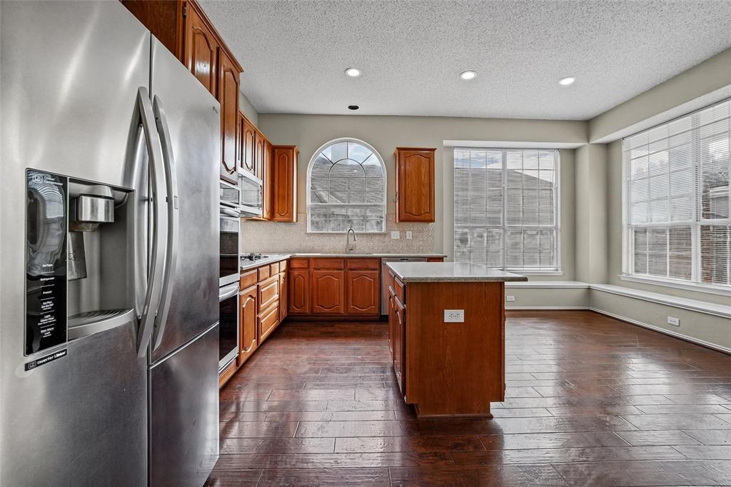 Kitchen featuring wood cabinetry, stainless steel double wall ovens, a central island, recessed lighting, and an arched window