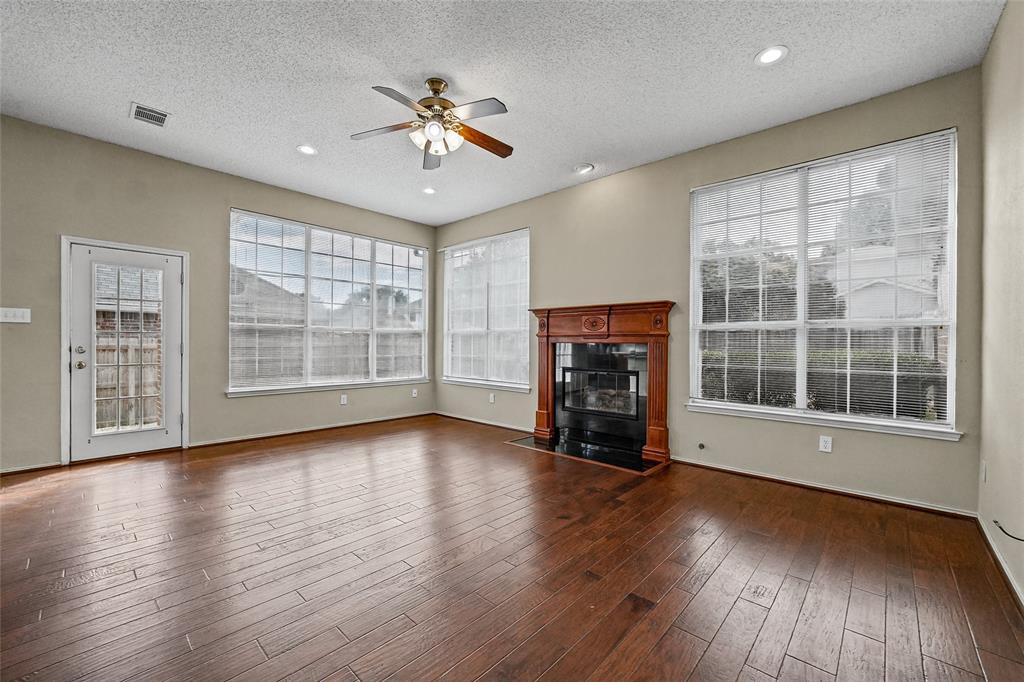 Wood-finish flooring, fireplace with a decorative mantel, multiple large windows, recessed lighting, and a ceiling fan
