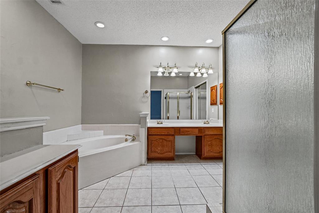 Bathroom featuring wood-finish cabinetry, a large soaking tub with tile surround, a double-sink vanity, recessed lighting, and tile flooring