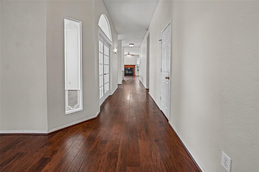 Interior hall featuring wood-finish flooring, white French doors with an arched transom, a vertical accent window, and a built-in fireplace with a mantel