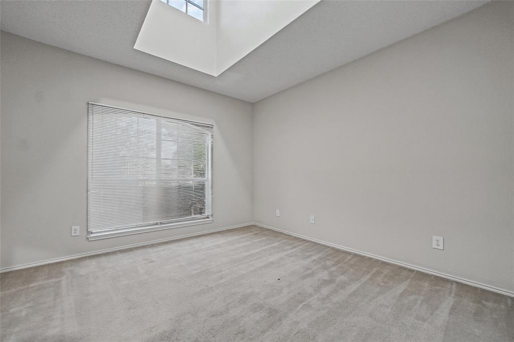 Neutral-toned interior space featuring a recessed skylight, wall-to-wall carpeting, and a large window with fitted blinds