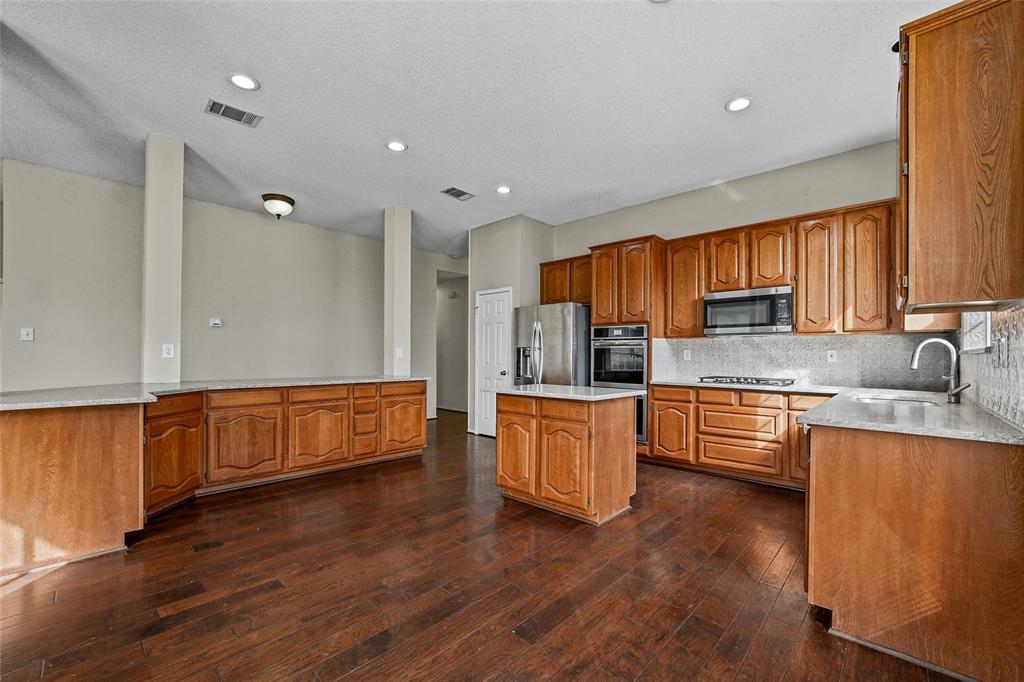 Kitchen featuring stained wood cabinetry, stone countertops, a center island, stainless steel wall-mounted oven and microwave, and wood-finish flooring