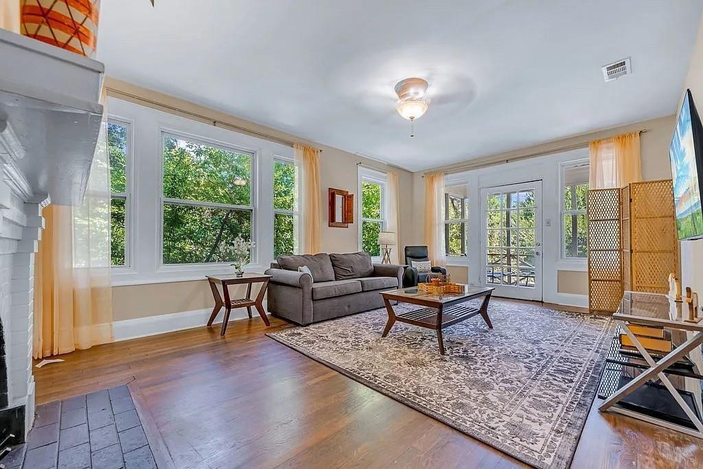 Living area featuring wood-finish flooring, a masonry fireplace, abundant windows, and a glass-paneled exterior door Living area featuring wood-finish flooring, a masonry fireplace, abundant windows, and a glass-paneled exterior door