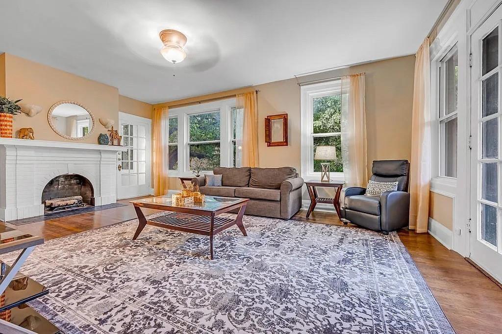 Living area featuring a white fireplace mantle, wood-finish flooring, multi-pane windows, and a glass-paned door Living area featuring a white fireplace mantle, wood-finish flooring, multi-pane windows, and a glass-paned door