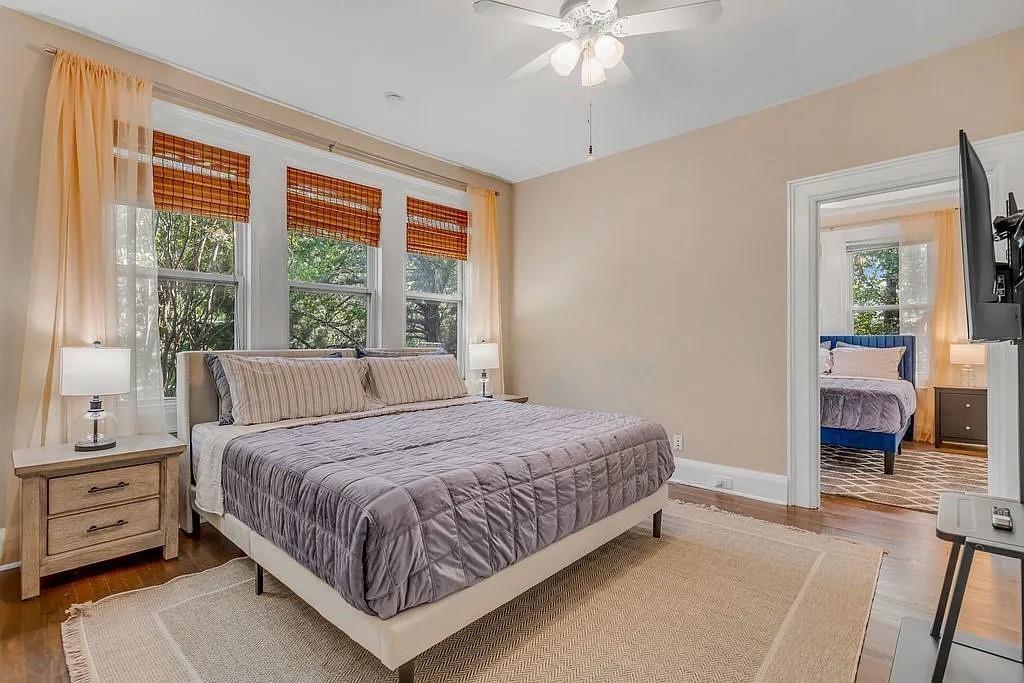 Spacious room featuring wood-finish flooring, a ceiling fan with integrated lighting, and a bank of three large windows