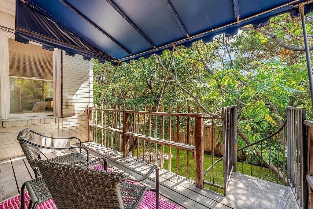 Elevated wood deck featuring a retractable blue fabric awning, wooden balustrade, and metal staircase