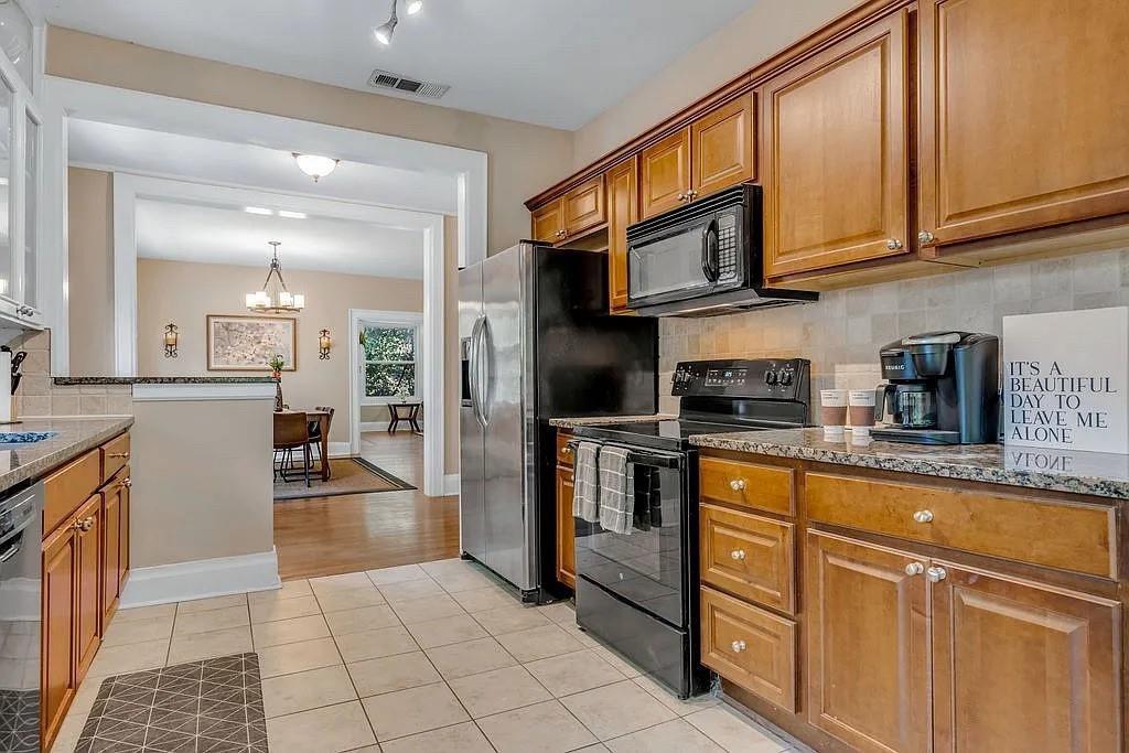 Kitchen featuring stained wood cabinetry, stone-finish countertops, tile flooring, and stainless steel appliances Kitchen featuring stained wood cabinetry, stone-finish countertops, tile flooring, and stainless steel appliances