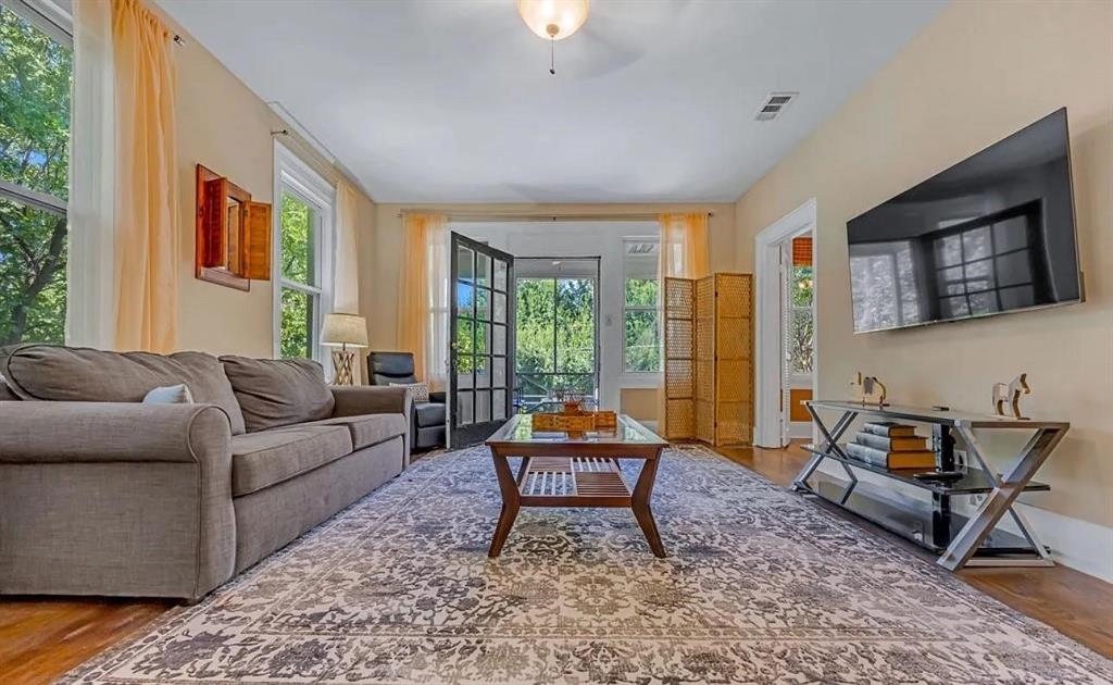 Living area featuring wood-finish flooring, high ceilings with central lighting, and multi-pane glass door access to a screened porch Living area featuring wood-finish flooring, high ceilings with central lighting, and multi-pane glass door access to a screened porch