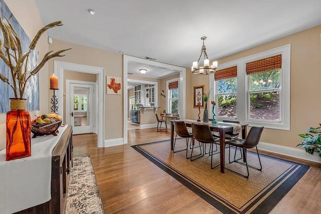 Dining area featuring wood-finish flooring, tall windows with woven shades, a multi-arm chandelier, and wide casing trim around openings Dining area featuring wood-finish flooring, tall windows with woven shades, a multi-arm chandelier, and wide casing trim around openings
