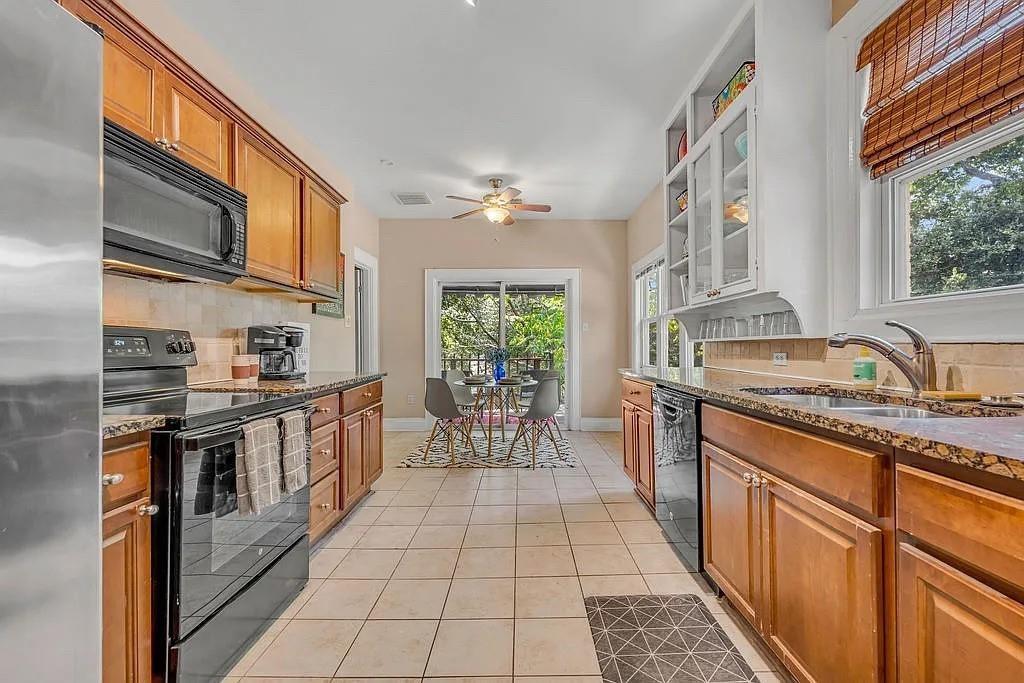 Kitchen featuring stained cabinetry, stone countertops, tile flooring, glass-front upper storage, and sliding glass doors Kitchen featuring stained cabinetry, stone countertops, tile flooring, glass-front upper storage, and sliding glass doors