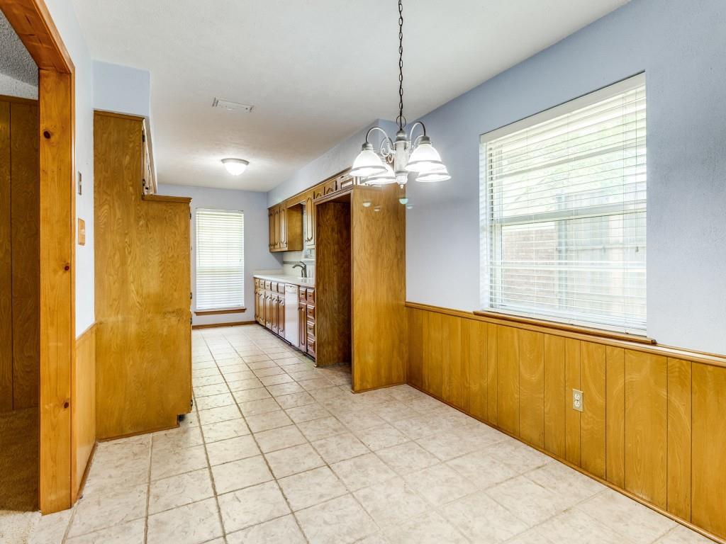 Kitchen featuring brown cabinets, a chandelier, a wainscoted wall, dishwasher, and wooden walls
