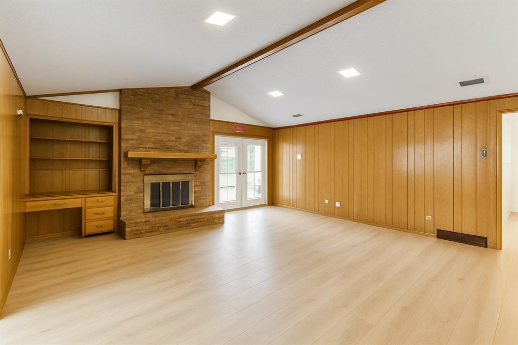 Unfurnished living room featuring light wood finished floors, wood walls, and a fireplace