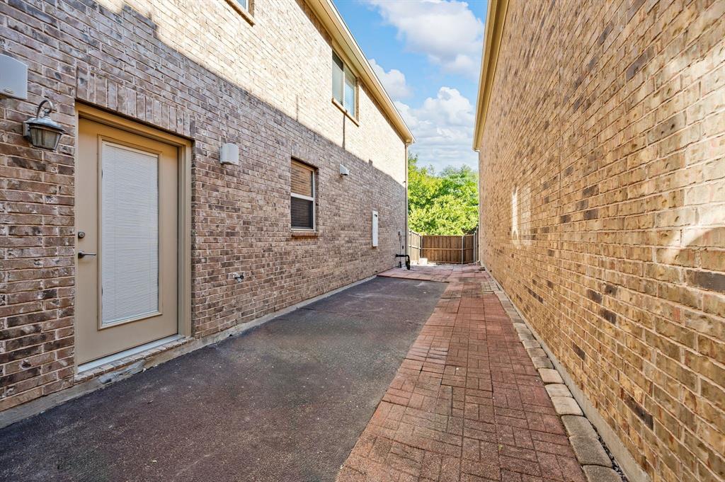 Multi-story brick exterior with a paved walkway, external lighting fixtures, and a recessed door