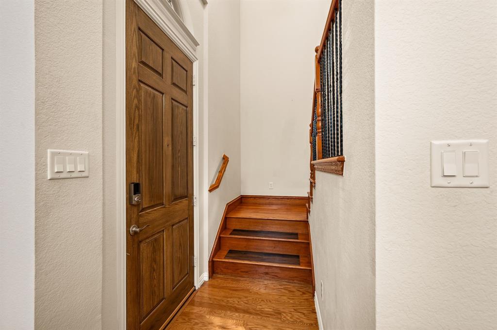Entryway featuring a solid wood door, wood-finish flooring, wood staircase treads, and decorative wrought iron balusters