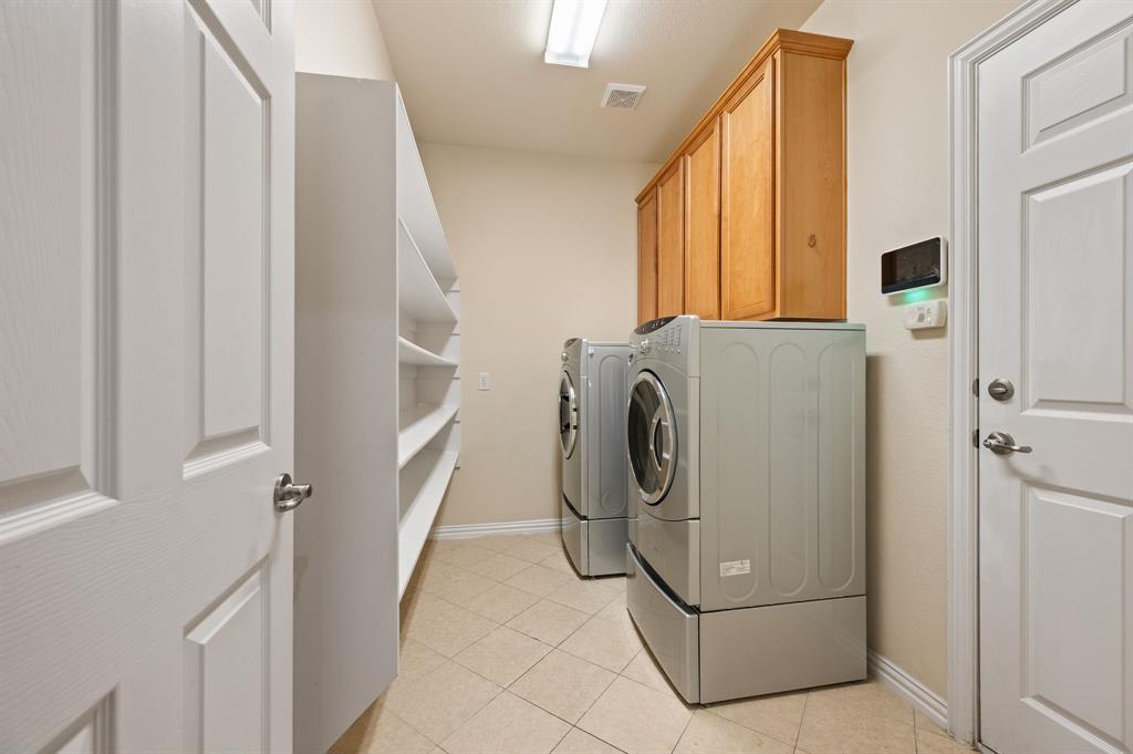 Dedicated utility space featuring light-toned tile flooring, built-in wooden cabinetry, expansive open shelving, and a ceiling-mounted light fixture