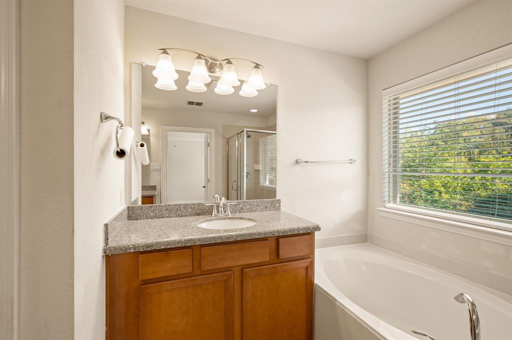 Bathroom vanity featuring a stone-composite countertop, undermount sink, multi-bulb light fixture, and deep-toned wood cabinetry, accompanied by a built-in soaking tub