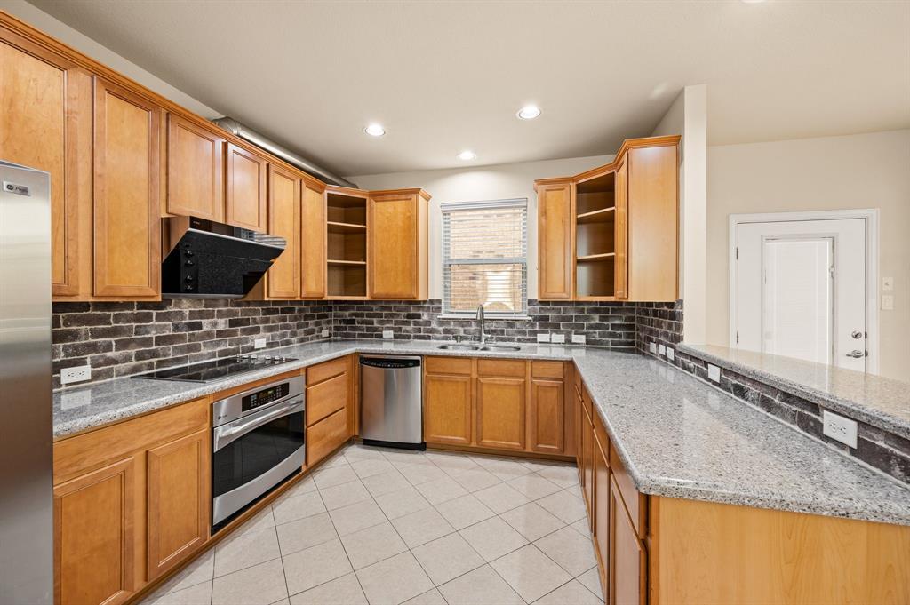 Kitchen featuring wood cabinetry, stone countertops, brick-style backsplash, stainless steel appliances, and tile flooring
