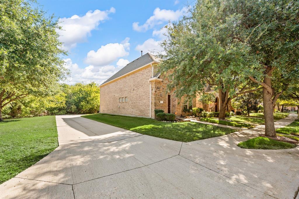 Brick exterior featuring a concrete driveway and mature trees on a landscaped lot
