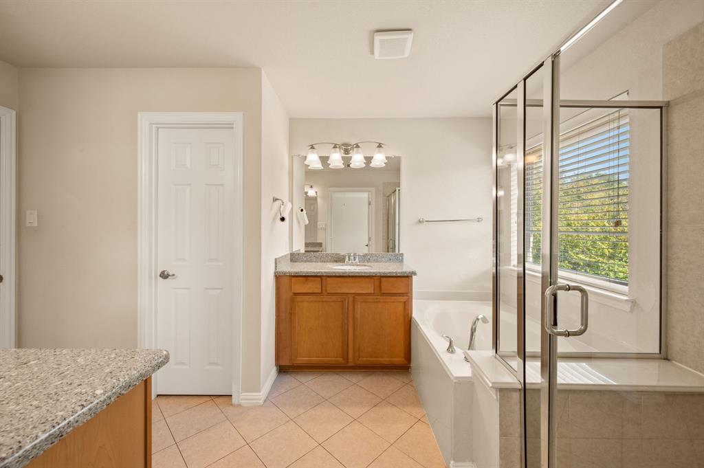 Bathroom featuring wood-finish cabinetry, stone-composite countertop with an integrated sink, glass-enclosed shower, soaking tub, and ceramic tile flooring