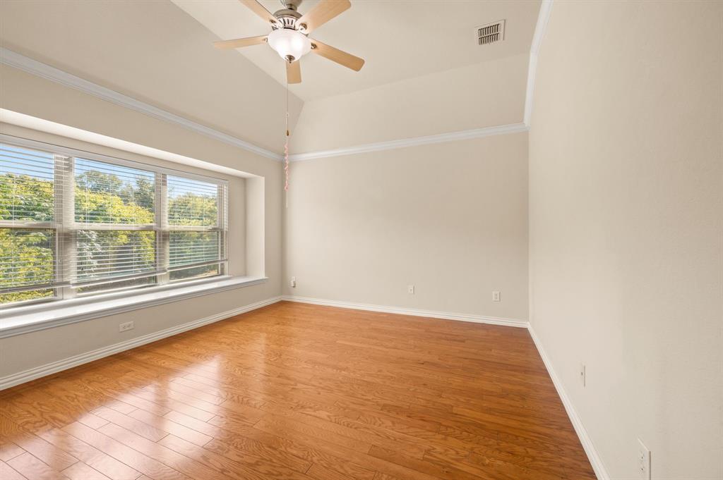 Vaulted ceilings with crown molding, wood-finish flooring, and a large bay window featuring an integrated window seat and ceiling fan