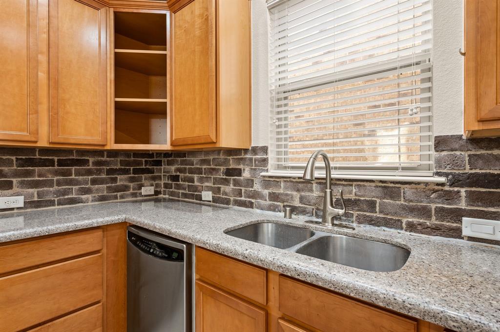 Kitchen area featuring stained wood cabinetry, stone-surface countertops, a dark-toned brick backsplash, a stainless steel double-basin undermount sink, and a high-arch pull-down faucet