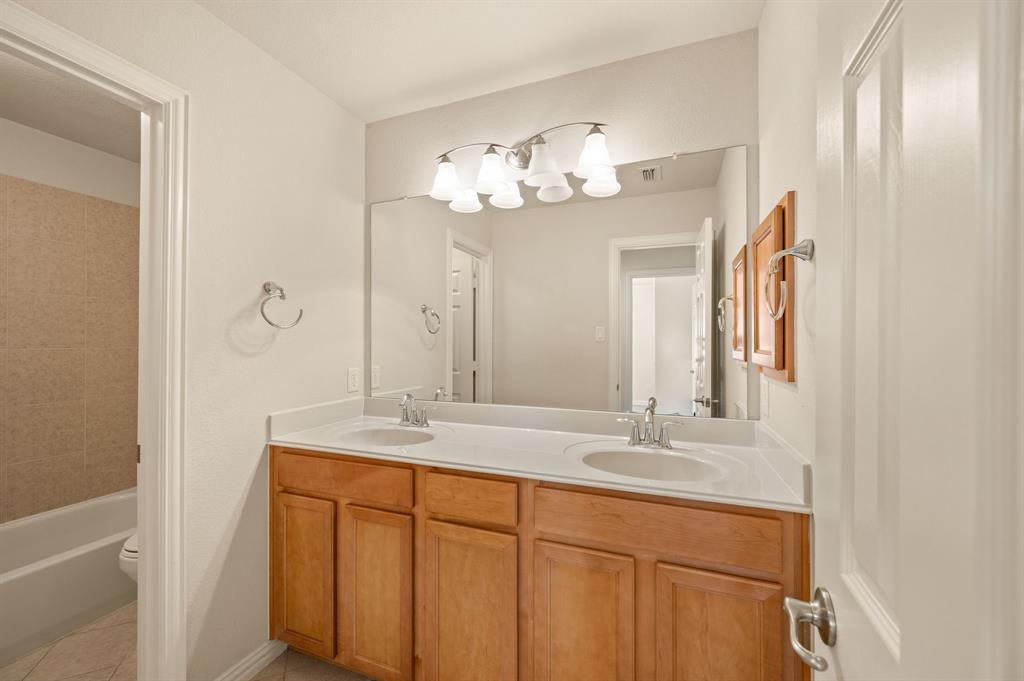 Bathroom featuring a double-sink vanity with wood cabinetry, a solid-surface countertop, an expansive wall-mounted mirror, and multi-bulb decorative lighting