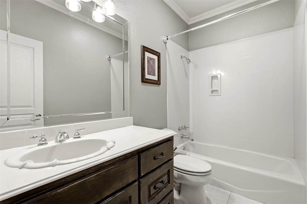 White ceramic vanity sink with chrome fixtures, dark wood-finish cabinetry, light countertop, and a white bathtub with shower