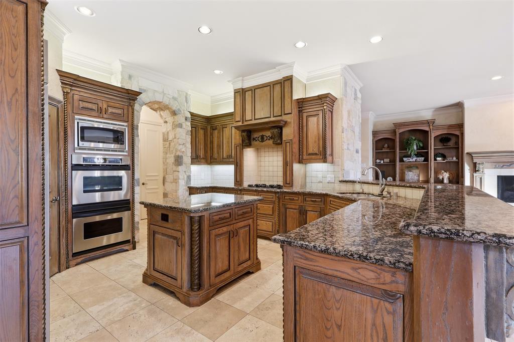 Kitchen featuring custom wood cabinetry, stone countertops, stainless steel appliances, a center island, and tile flooring