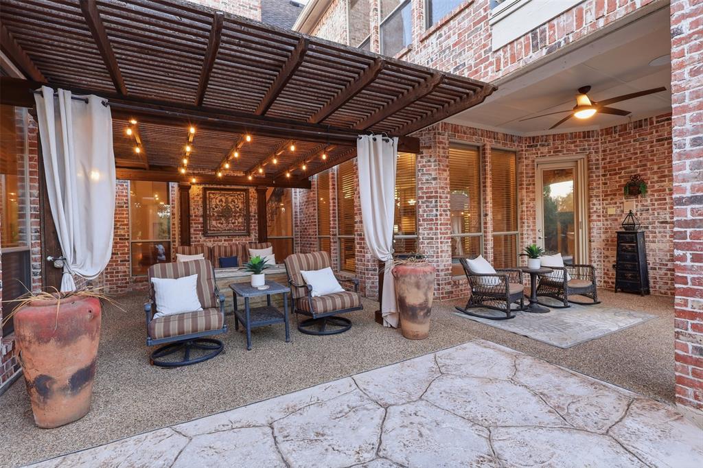 Covered patio featuring a wood-slat pergola, string lighting, exposed brick walls, a ceiling fan, and textured concrete flooring