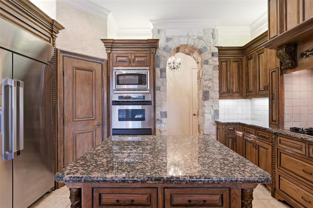 Gourmet kitchen featuring a granite-topped island, rich wood cabinetry, stainless steel appliances, a stone archway, and tile backsplash