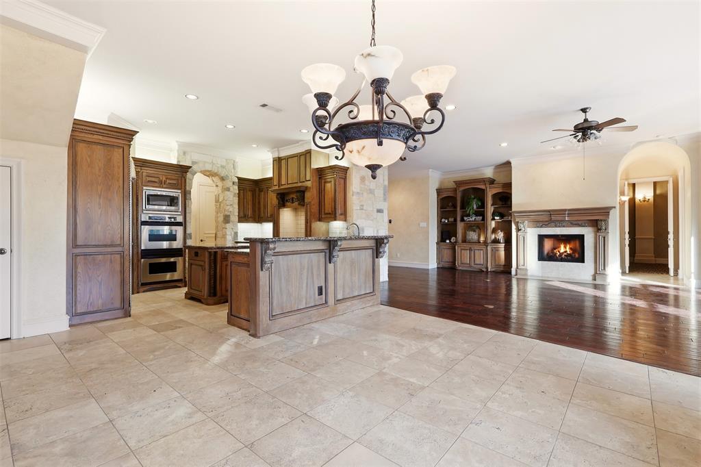 Stone tile flooring, wood-finish cabinetry, stainless steel double oven, built-in shelving, and a stone fireplace with a wood-finish mantel