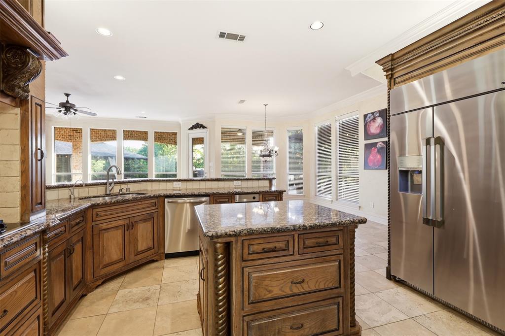 Kitchen featuring stone tile flooring, granite countertops, wood cabinetry, a center island with storage, and a stainless steel refrigerator
