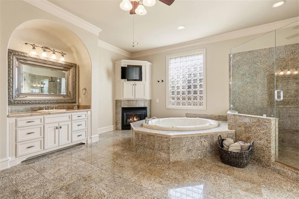 Spacious bathroom featuring a jetted tub with polished chrome fixtures, a walk-in shower with glass enclosure and tiled surround, a vanity with ample storage and a framed mirror, and light-toned tile flooring