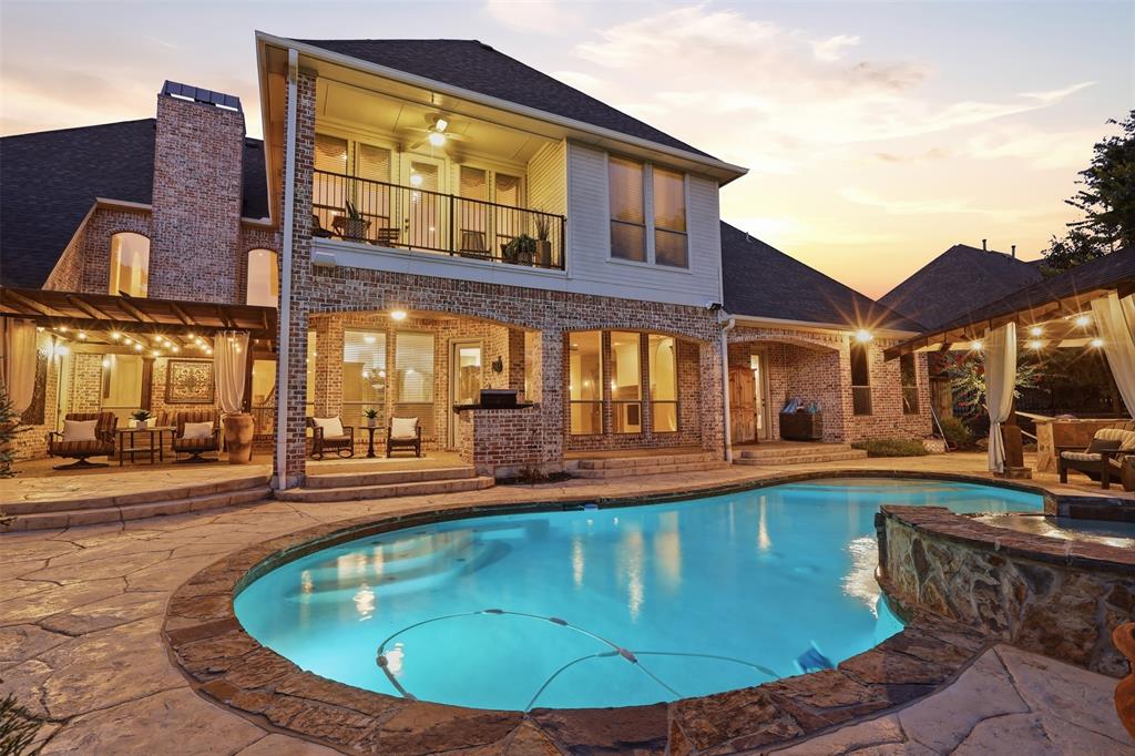 Rear exterior featuring a stone patio, built-in swimming pool, covered outdoor living area, and a second-story balcony Rear exterior featuring a stone patio, built-in swimming pool, covered outdoor living area, and a second-story balcony