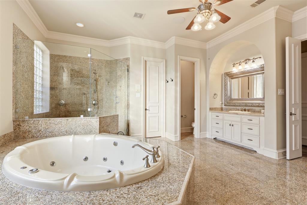 Spacious bathroom featuring a jetted tub with polished chrome fixtures, a walk-in shower with glass enclosure and tiled surround, a vanity with ample storage and a framed mirror, and light-toned tile flooring