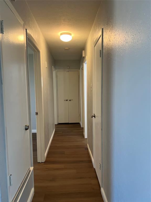 Hallway featuring wood-finish flooring, neutral wall paint, and multiple interior doors with metal hardware Hallway featuring wood-finish flooring, neutral wall paint, and multiple interior doors with metal hardware